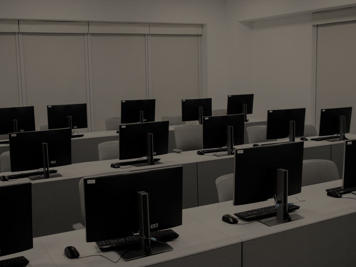 Una sala de cómputo vacía y a oscuras, con filas de computadores apagados.